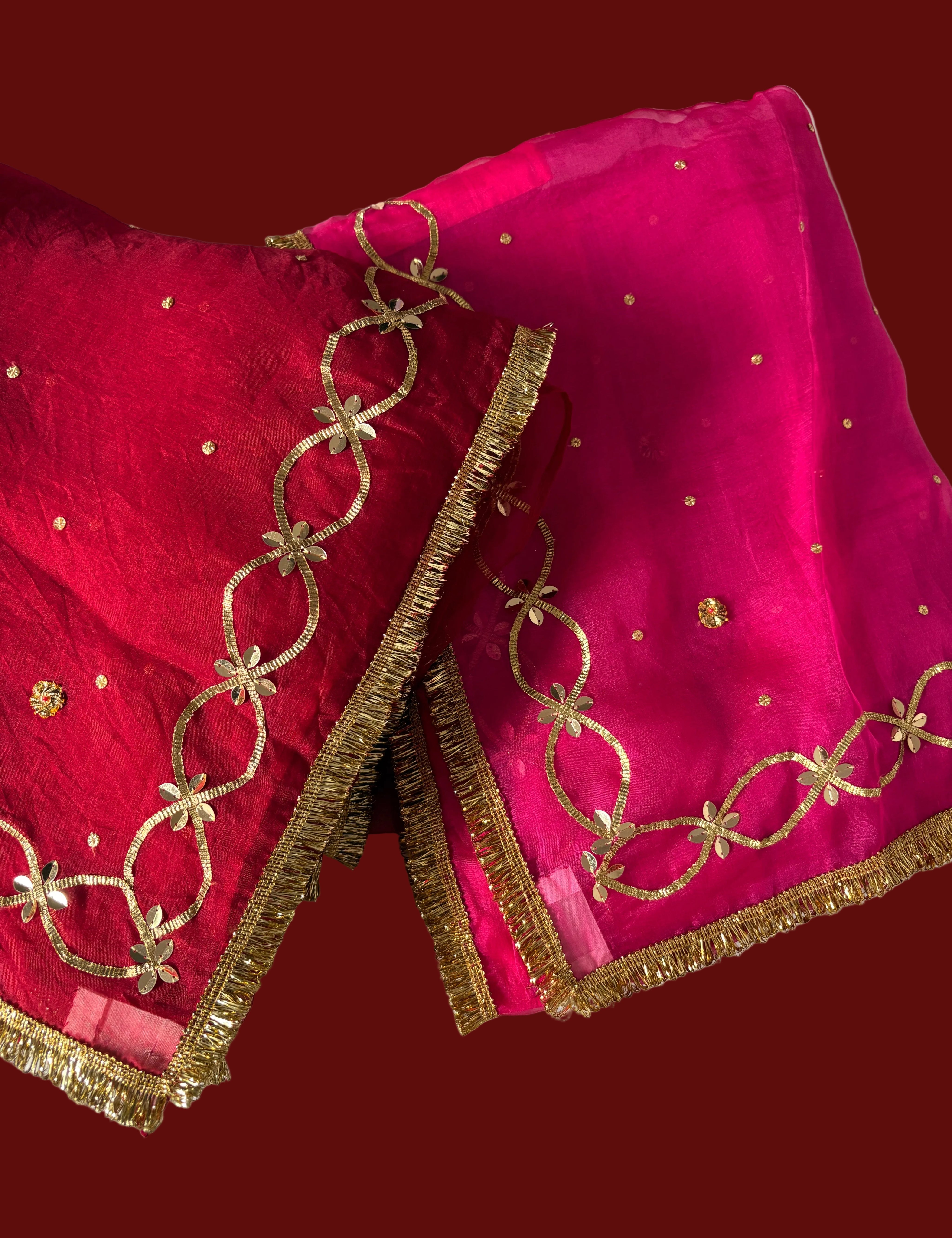 A close-up of a bright pink and red Saree, featuring gold floral embroidery, a gold fringe border by House of baisa