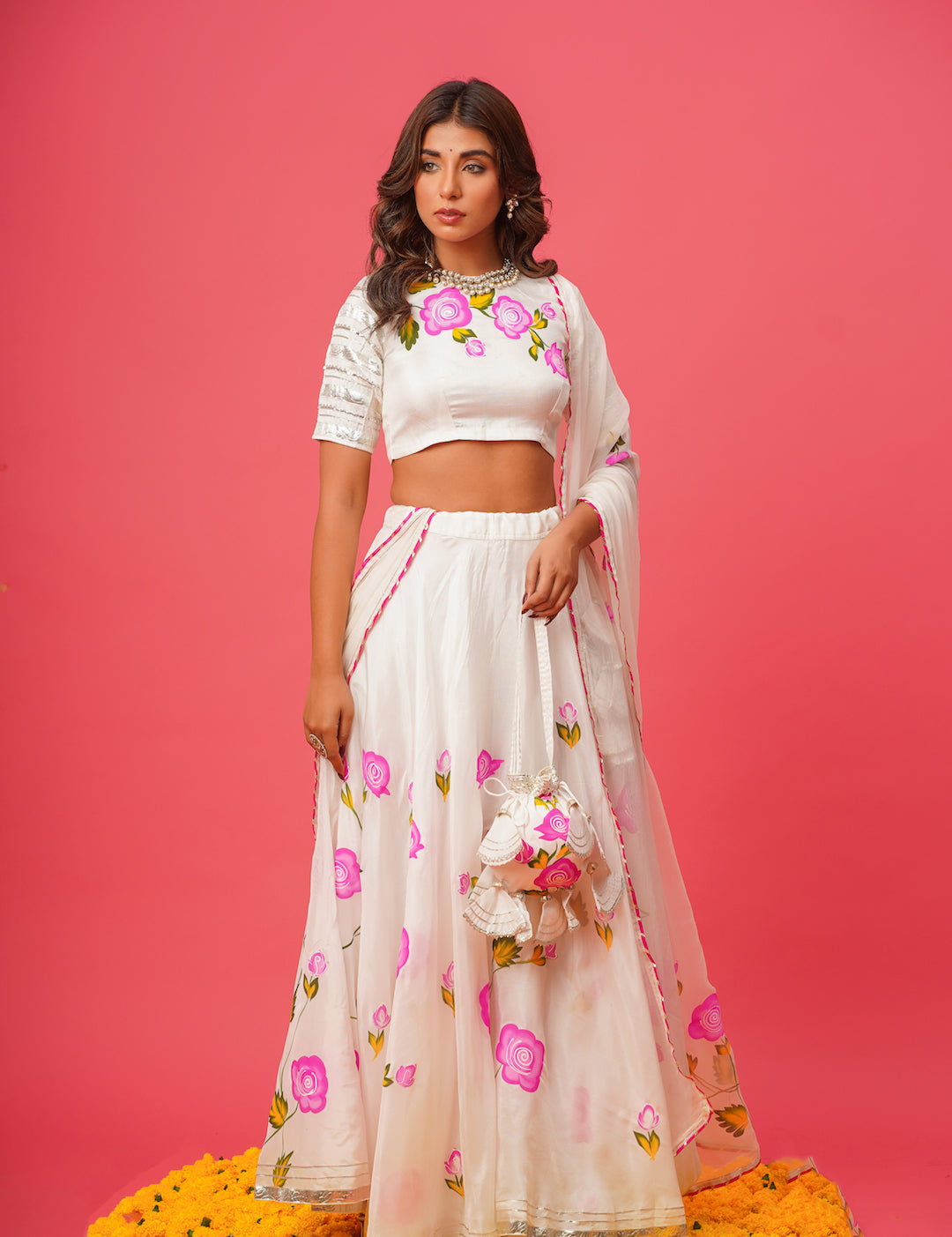 Elegant white lehenga set featuring hand-embroidered pink flowers and matching potli bag
