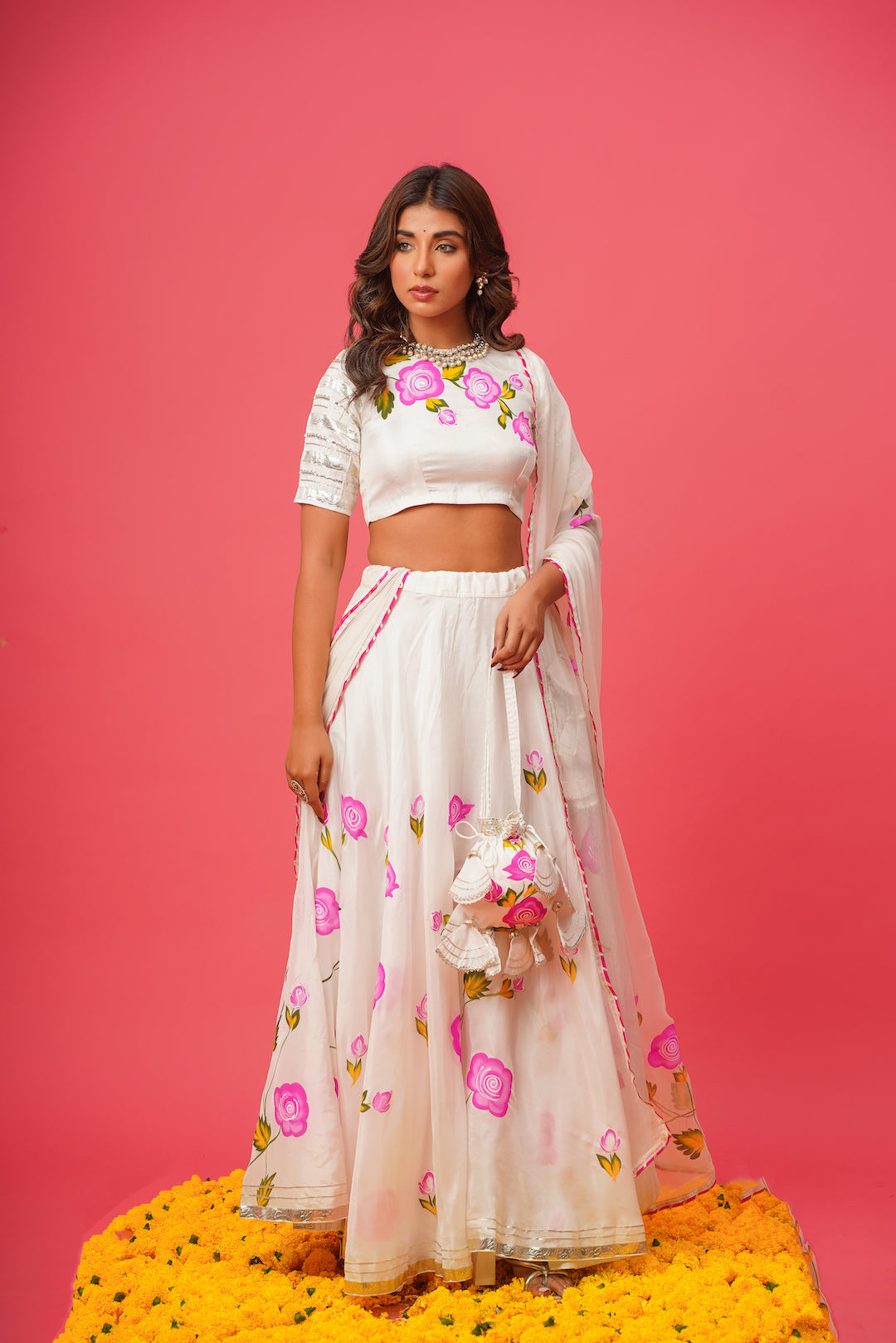 Elegant white lehenga set featuring hand-embroidered pink flowers and matching potli bag
