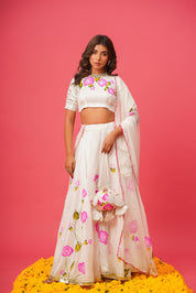 Model in white floral lehenga with pink rose embroidery on blouse and skirt
